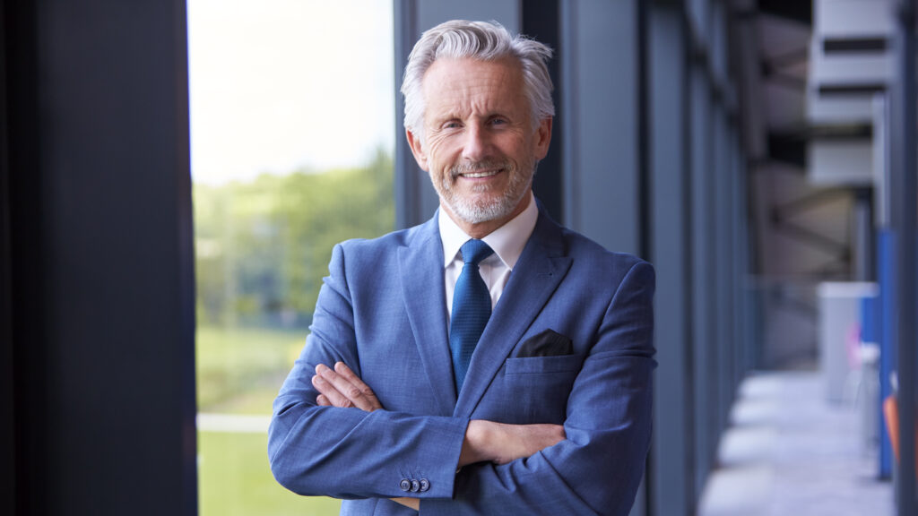 portrait of smiling senior businessman ceo chairman standing inside modern office building